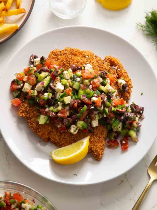 crispy greek chicken served on white plate with wedge of lemon