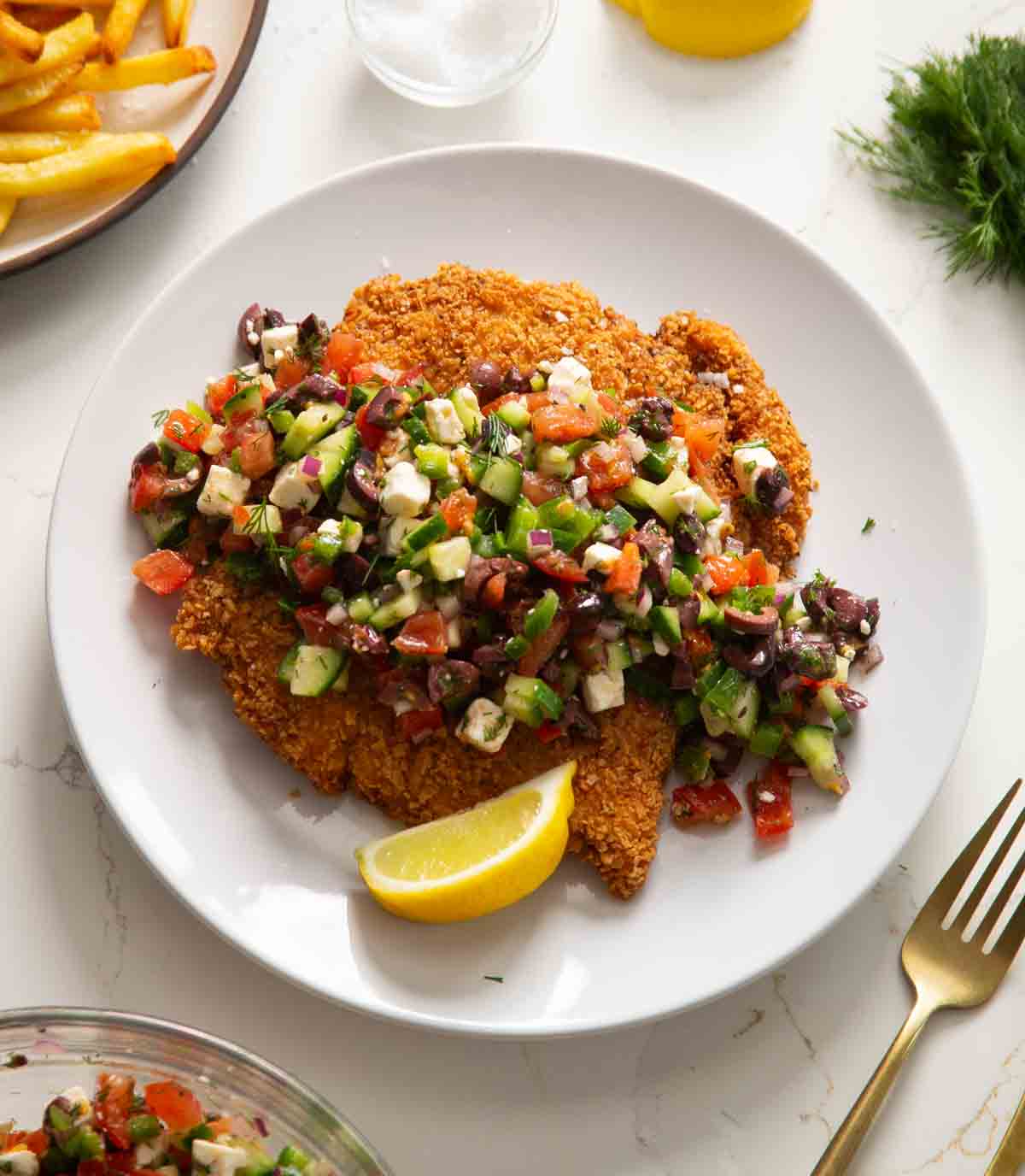 crispy greek chicken served on white plate with wedge of lemon