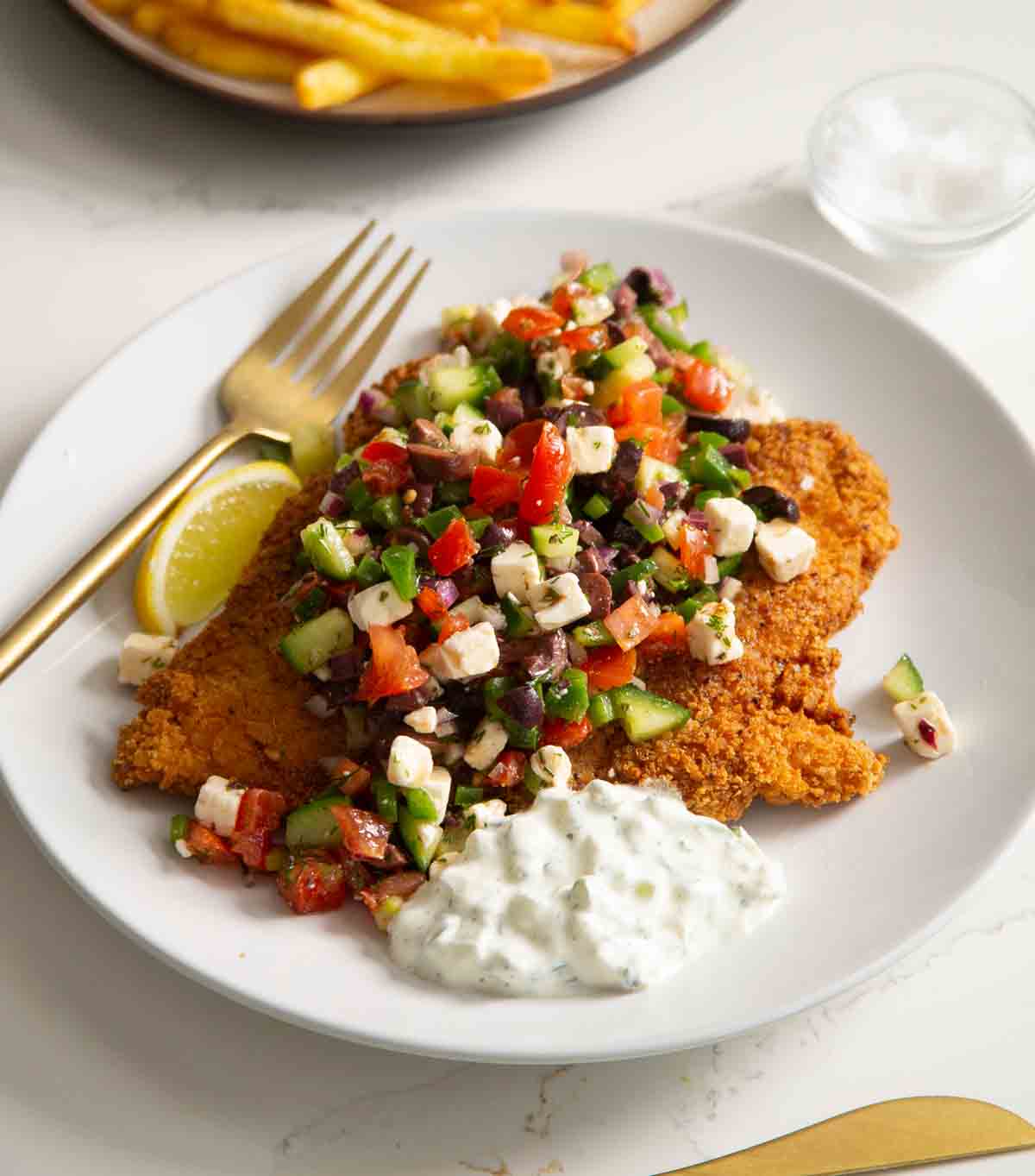 crispy greek chicken on white plate with tzatziki