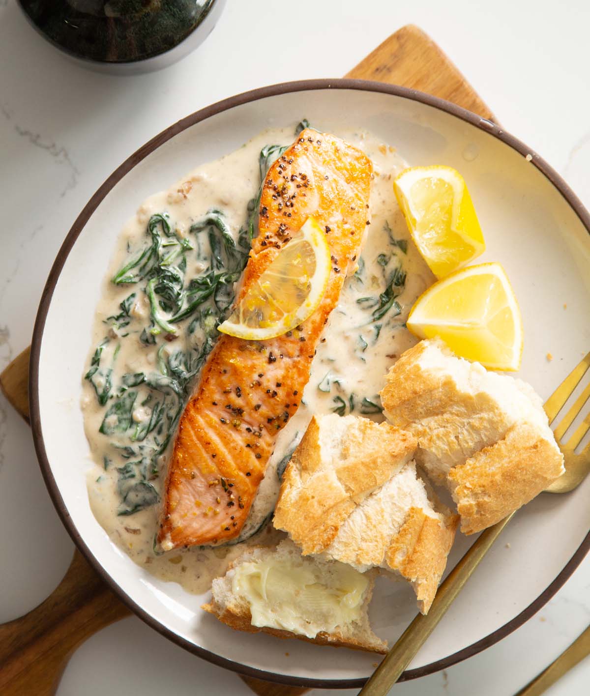 overhead shot of salmon fillet of spinach sauce with crusty bread on small white plate