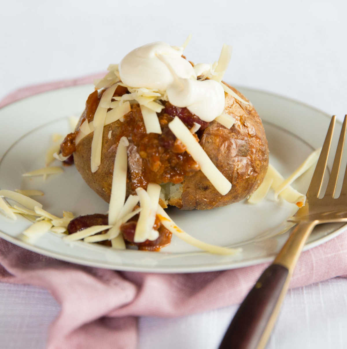 baked potato with chilli on small white plate on pink napkin