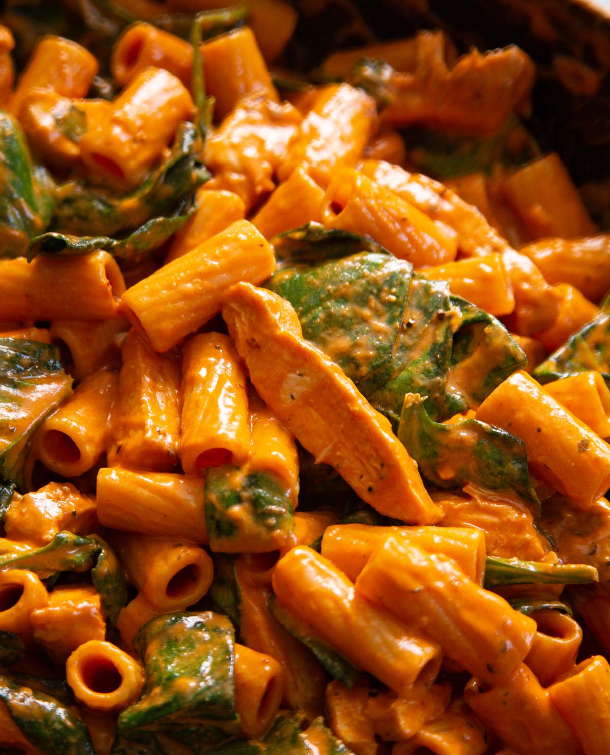 close up shot of chicken rigatoni in large pan with wooden spoon