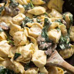 close up shot of wooden spoon digging into tortellini in pan