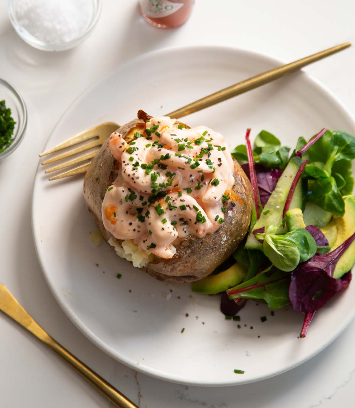 jacket potato with prawns on small white plate with gold cutlery and small side salad