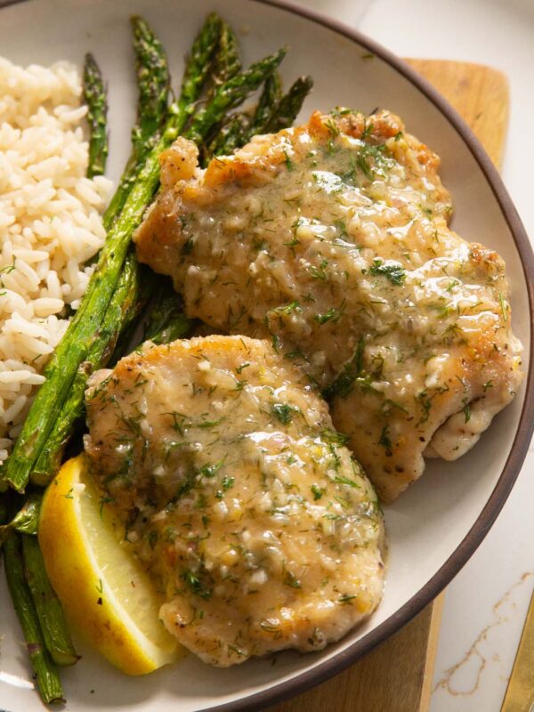 2 chicken thighs on small white plate with rice and asparagus and lemon wedge