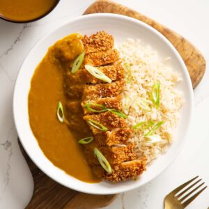 overhead shot of pork katsu curry on white plate on wooden chopping board