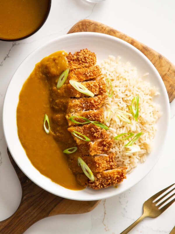 overhead shot of pork katsu curry on white plate on wooden chopping board