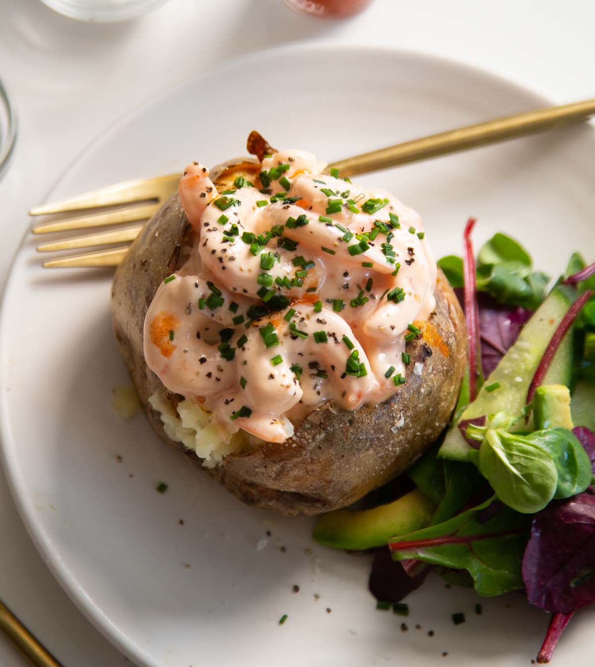 prawn baked potato on small white plate with salad and gold fork