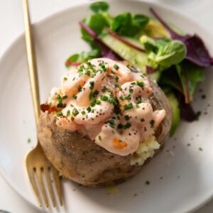 prawn jacket potato on small white plate with gold fork and side salad