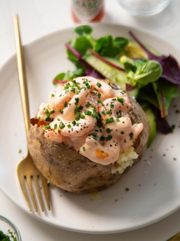 prawn jacket potato on small white plate with gold fork and side salad