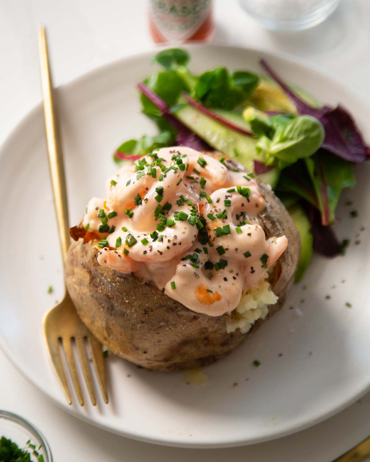 prawn jacket potato on small white plate with gold fork and side salad