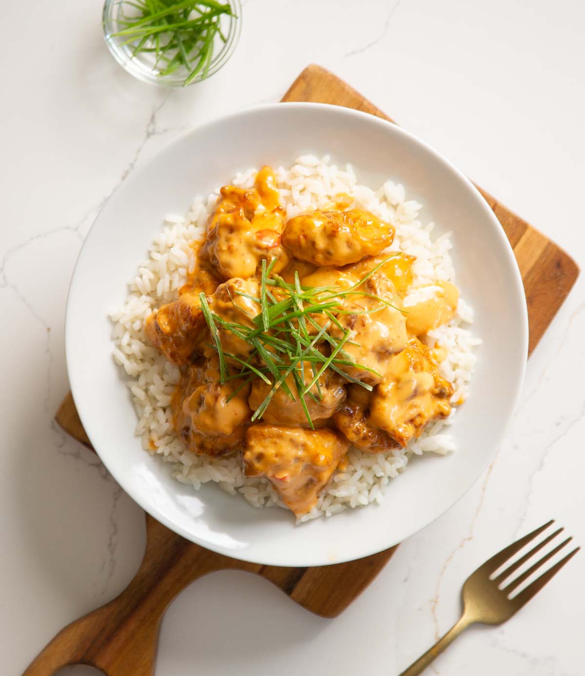 overhead shot of bang bang chicken in large white dish on chopping board with gold fork