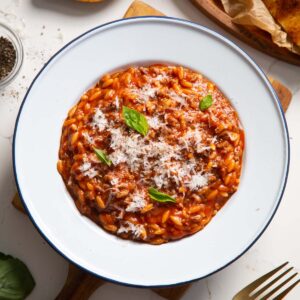overhead shot of beef orzo in white dish on wooden chopping board garnished with basil and parmesan