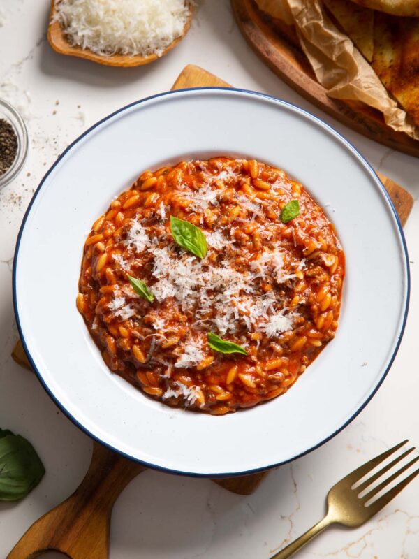 overhead shot of beef orzo in white dish on wooden chopping board garnished with basil and parmesan