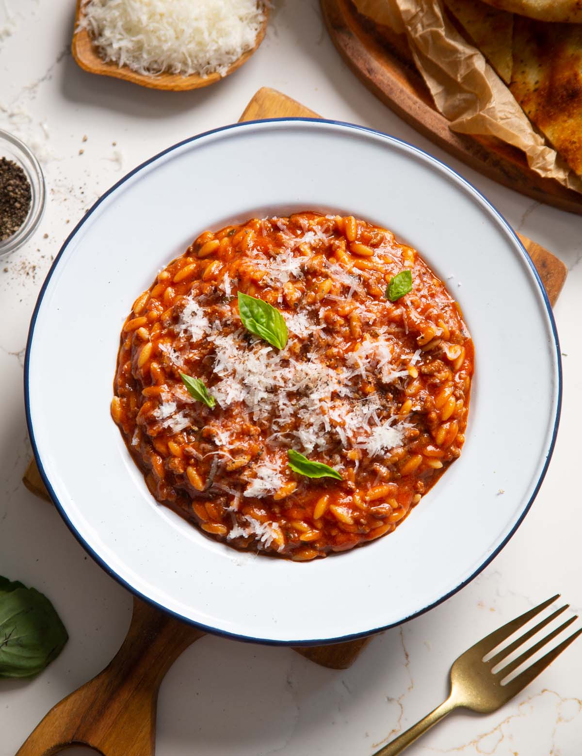overhead shot of beef orzo in white dish on wooden chopping board garnished with basil and parmesan