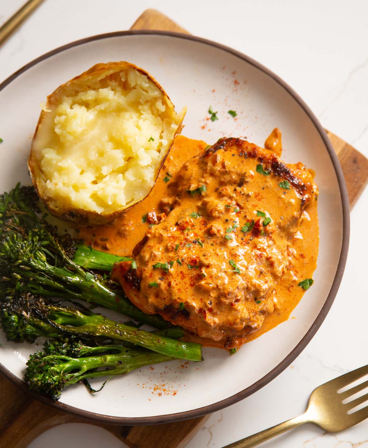 creamy paprika chicken on small white plate with potato and broccolini