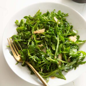 close up shot of rocket salad in white bowl with gold fork