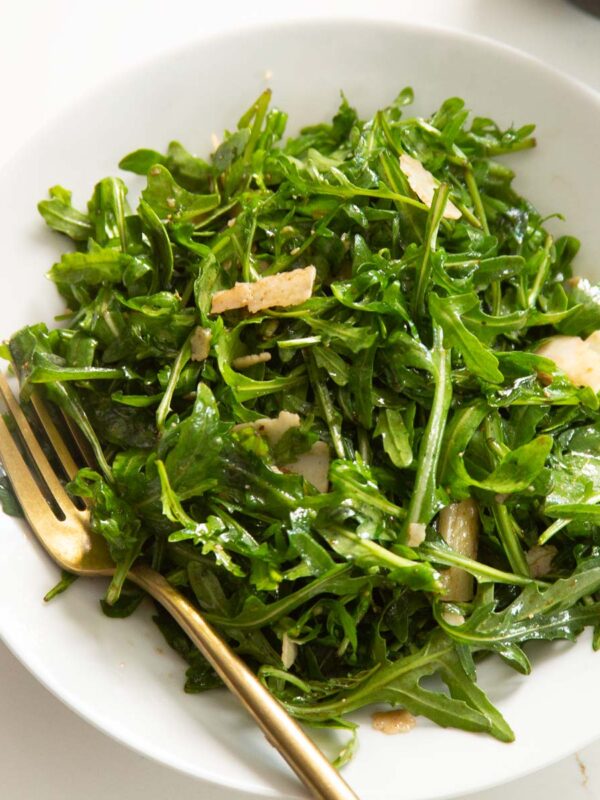 close up shot of rocket salad in white bowl with gold fork