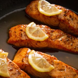 close up shot of 4 salmon fillets in pan garnished with lemon