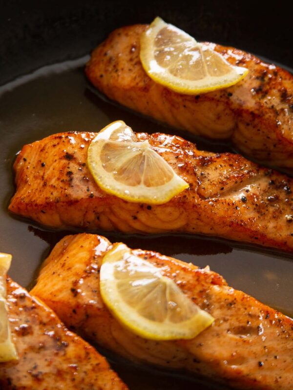 close up shot of 4 salmon fillets in pan garnished with lemon