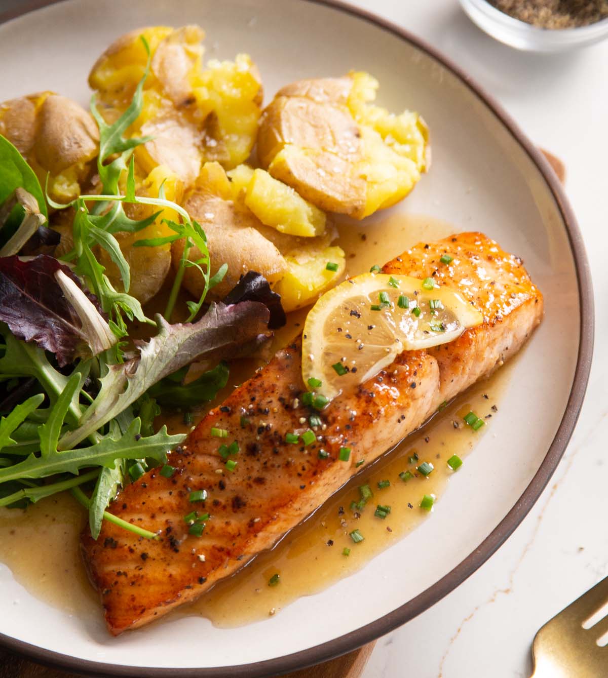 lemon honey salmon served on small white plate with potatoes and salad