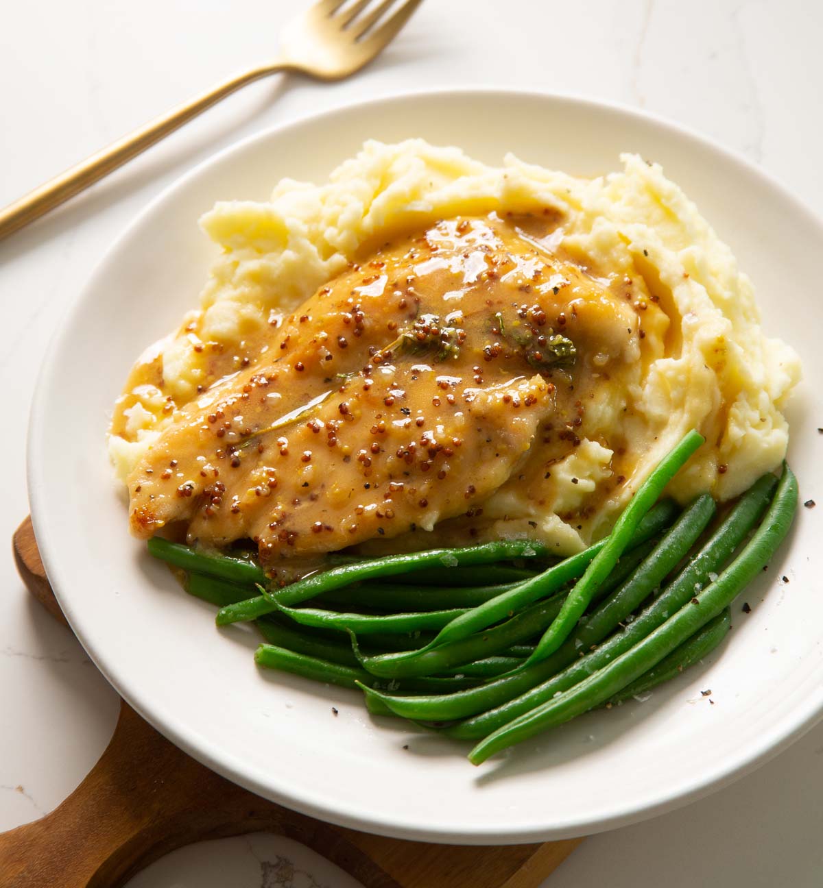 mustard honey chicken on mashed potato with green beans on small white plate