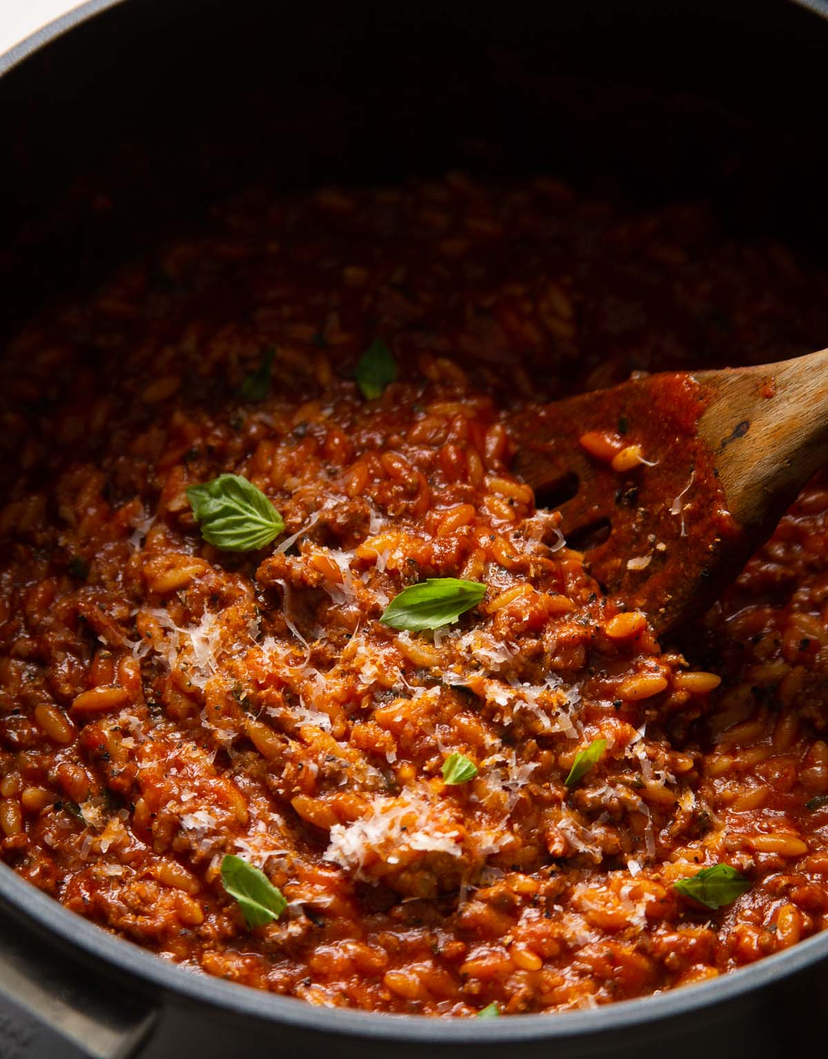 close up shot of beef orzo in large pot with wooden spoon garnished with basil