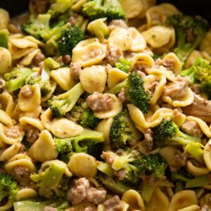 close up shot of wooden spoon digging into skillet of sausage and broccoli pasta