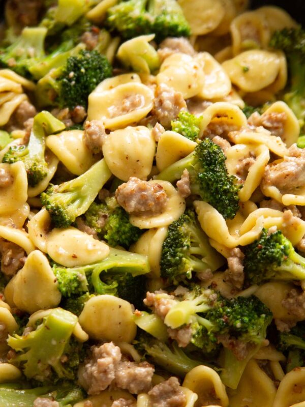 close up shot of wooden spoon digging into skillet of sausage and broccoli pasta