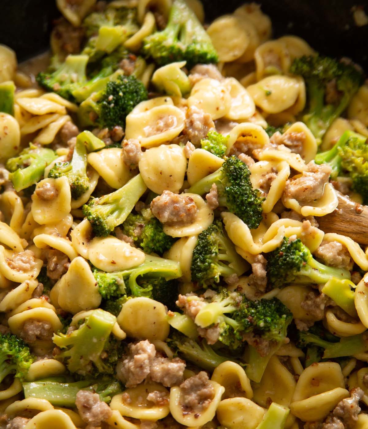 sausage and broccoli pasta in skillet with wooden spoon digging in