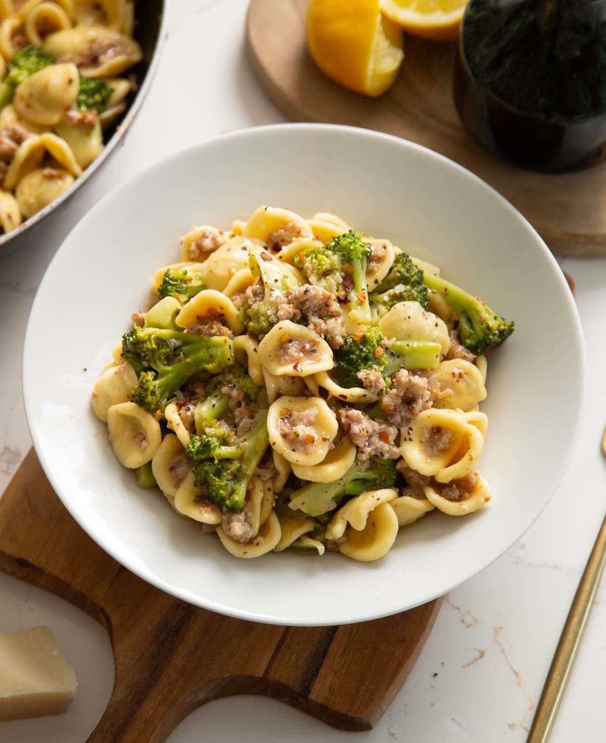 sausage broccoli pasta served in white dish on wooden chopping board