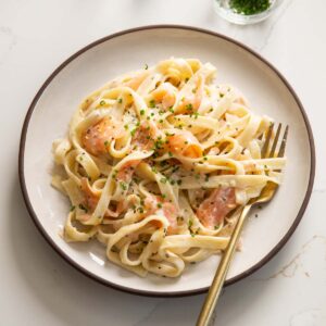 smoked salmon pasta served on small white plate with gold fork