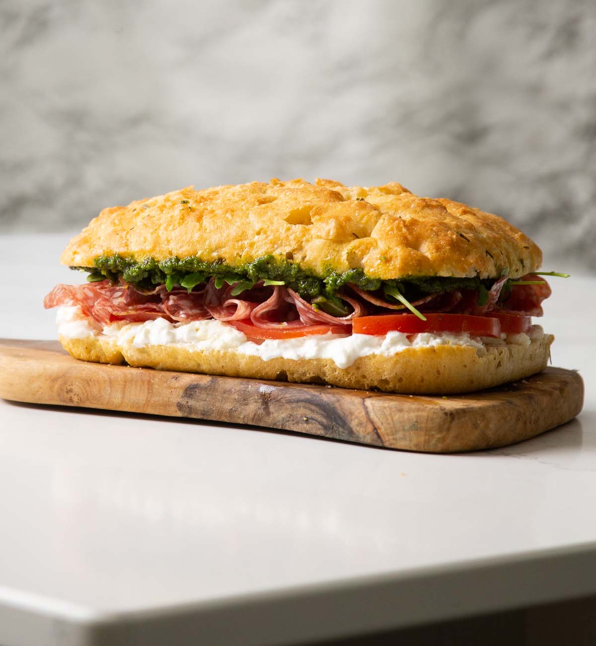 side shot of a large focaccia sandwich on chopping board on marble island