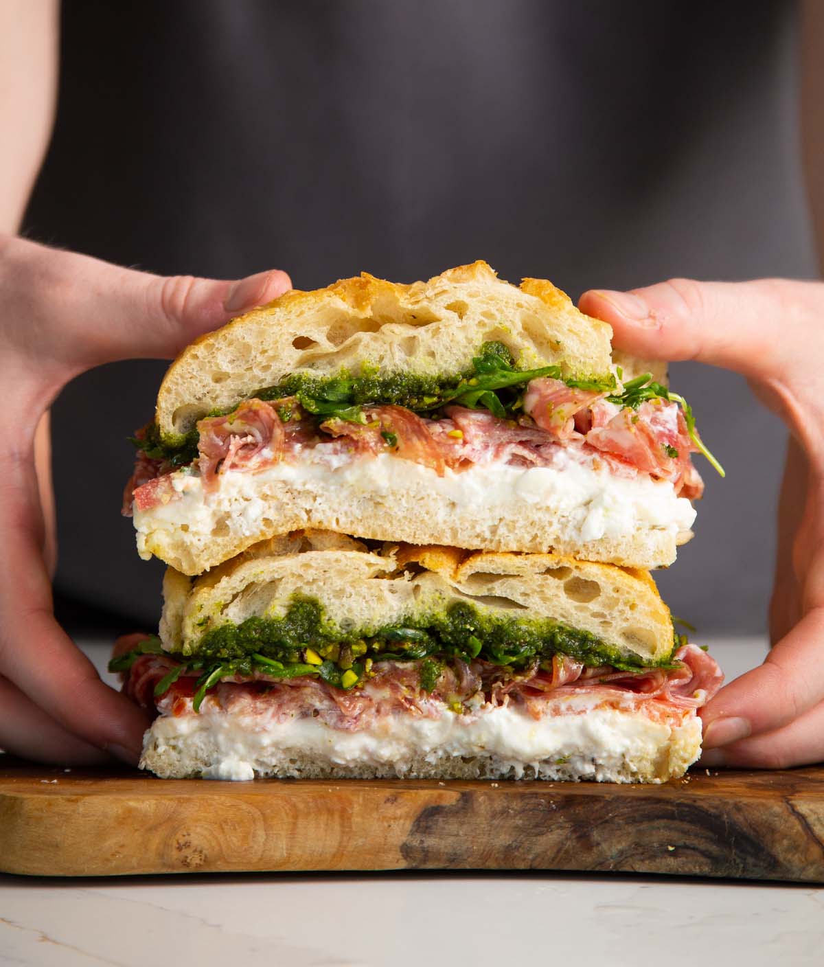hands holding focaccia sandwiches sliced in half showing filling