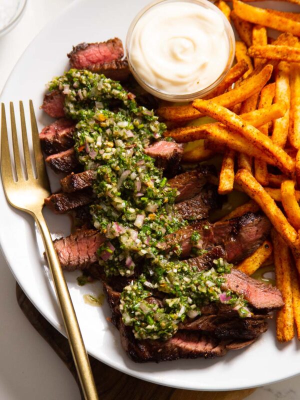 close up shot of steak and chimichurri served with fried on white plate with gold fork