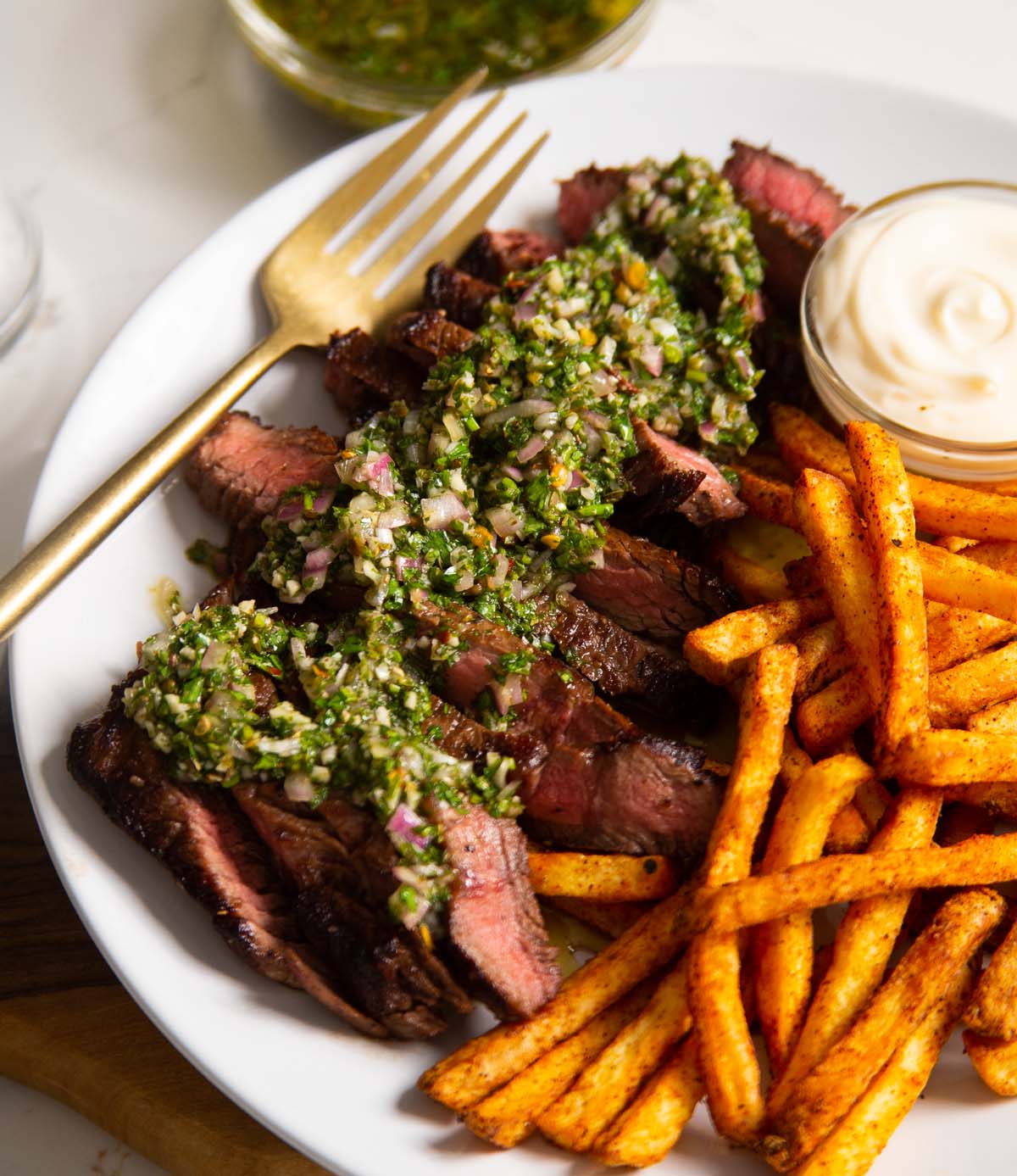 close up shot of chimichurri steak on plate with fries, dip and gold fork