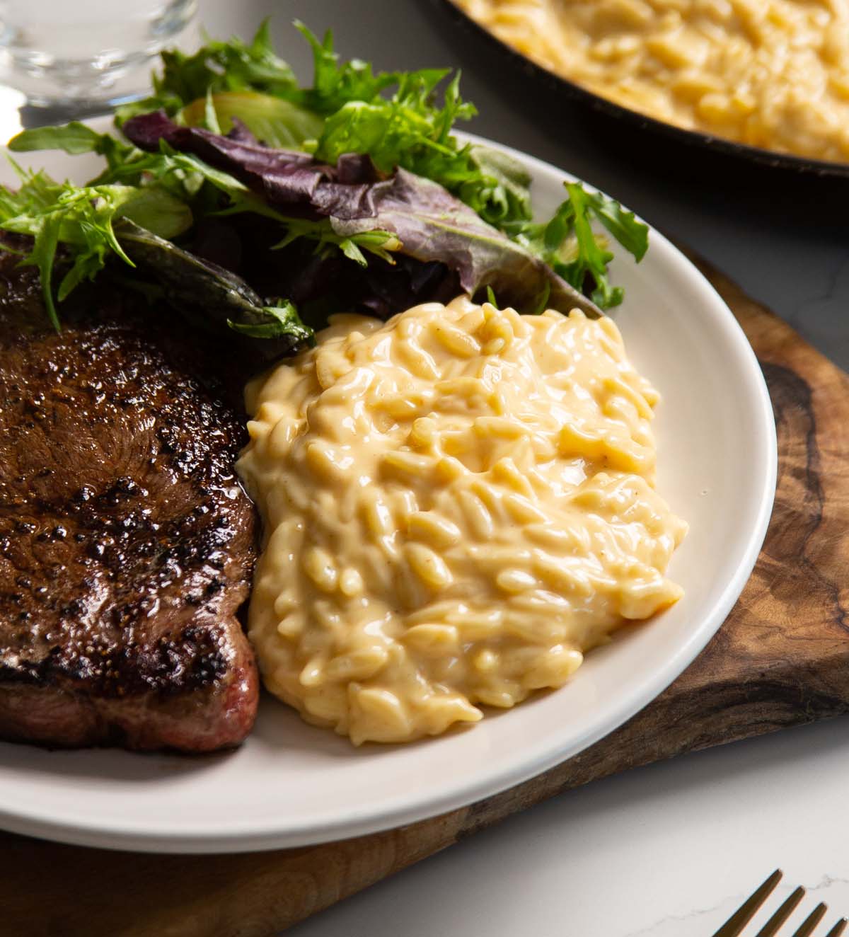 cheesy orzo served on white plate with steak and salad