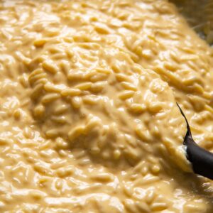 close up of cheesy orzo in pan with serving spoon