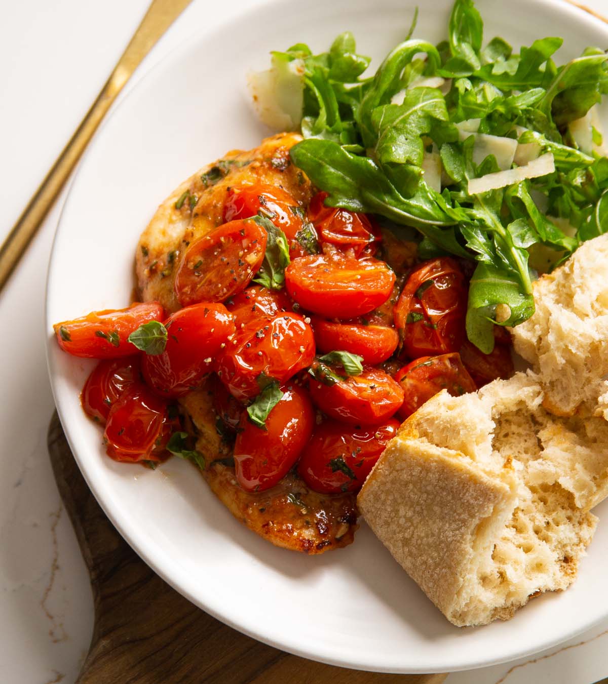 tomato basil chicken served on small white plate with salad and bread