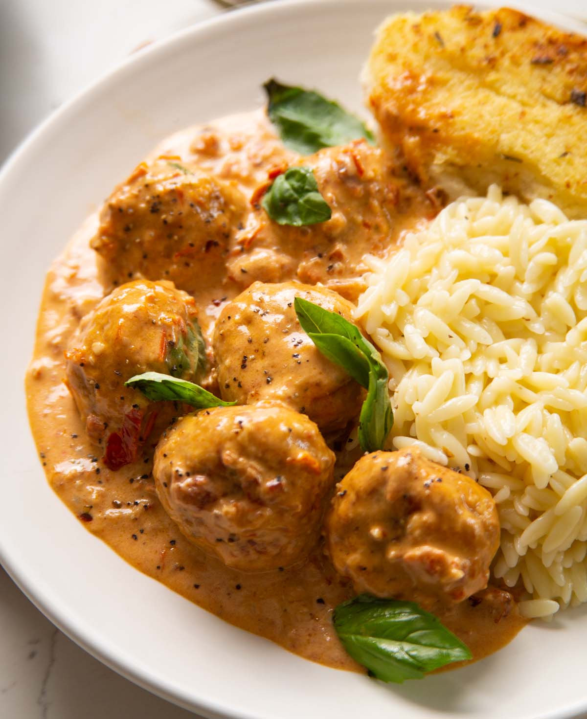 marry me chicken meatballs on small white plate with orzo and garlic bread