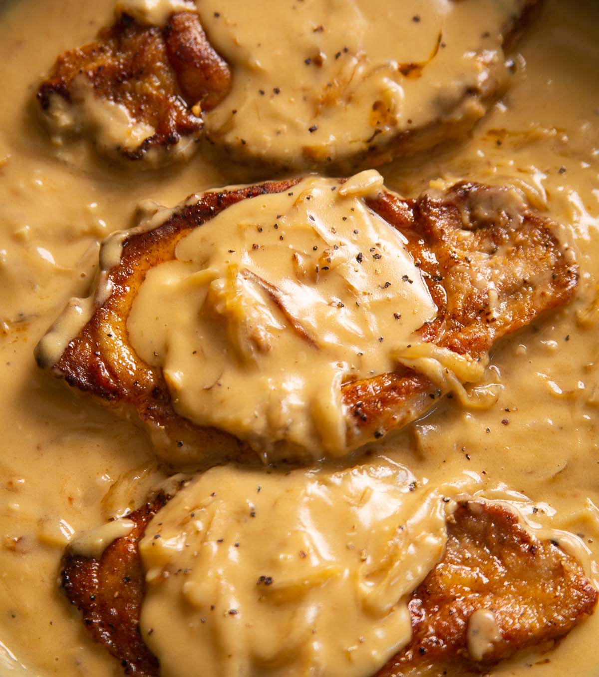 smothered pork chops in pan garnished with black pepper