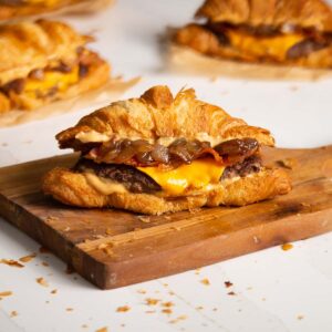 side shot of croissant smash burger on wooden chopping board