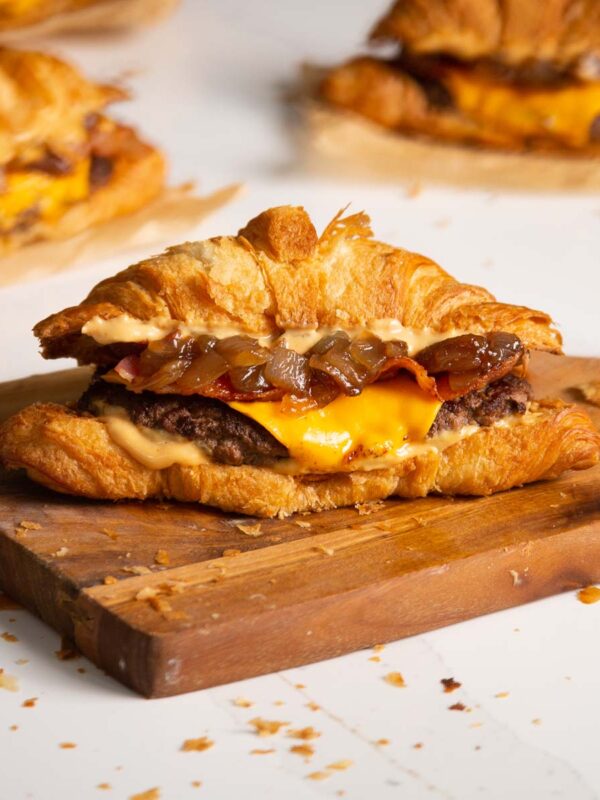 side shot of croissant smash burger on wooden chopping board