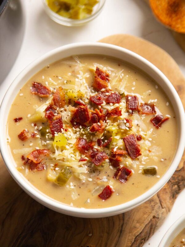 close up shot of cheeseburger soup in white bowl on wooden chopping board