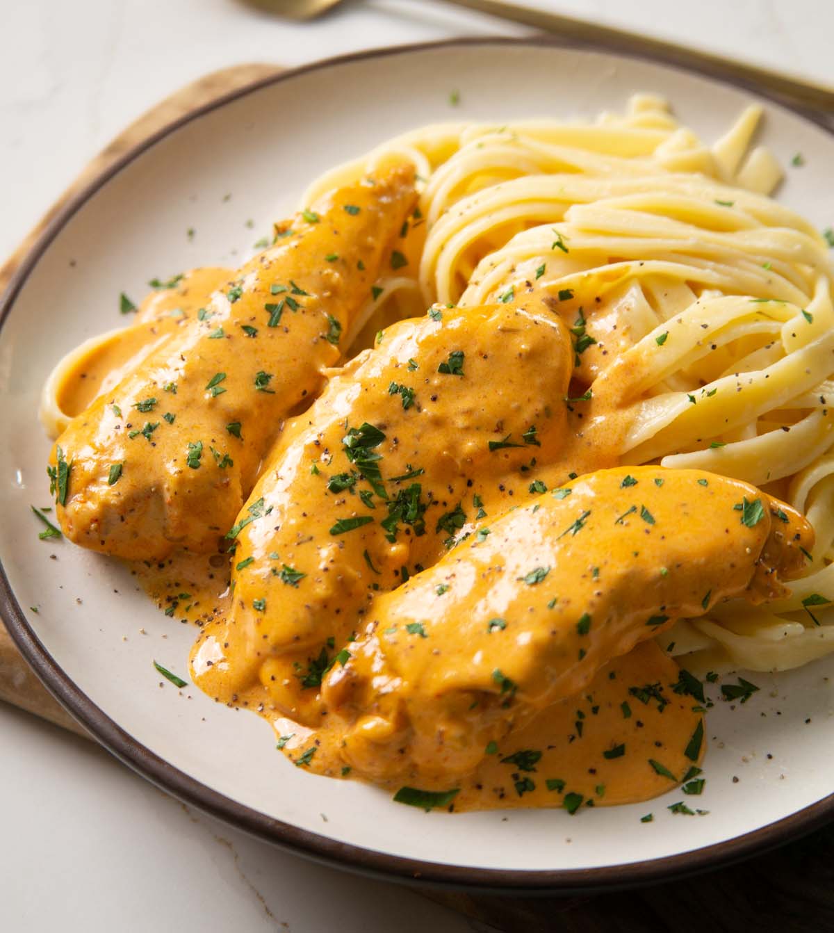 close up shot of chicken lazone on small white plate with fettuccine