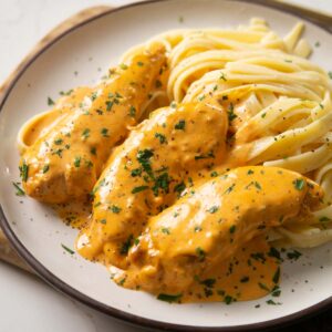 close up shot of chicken lazone with buttered noodles on small white plate