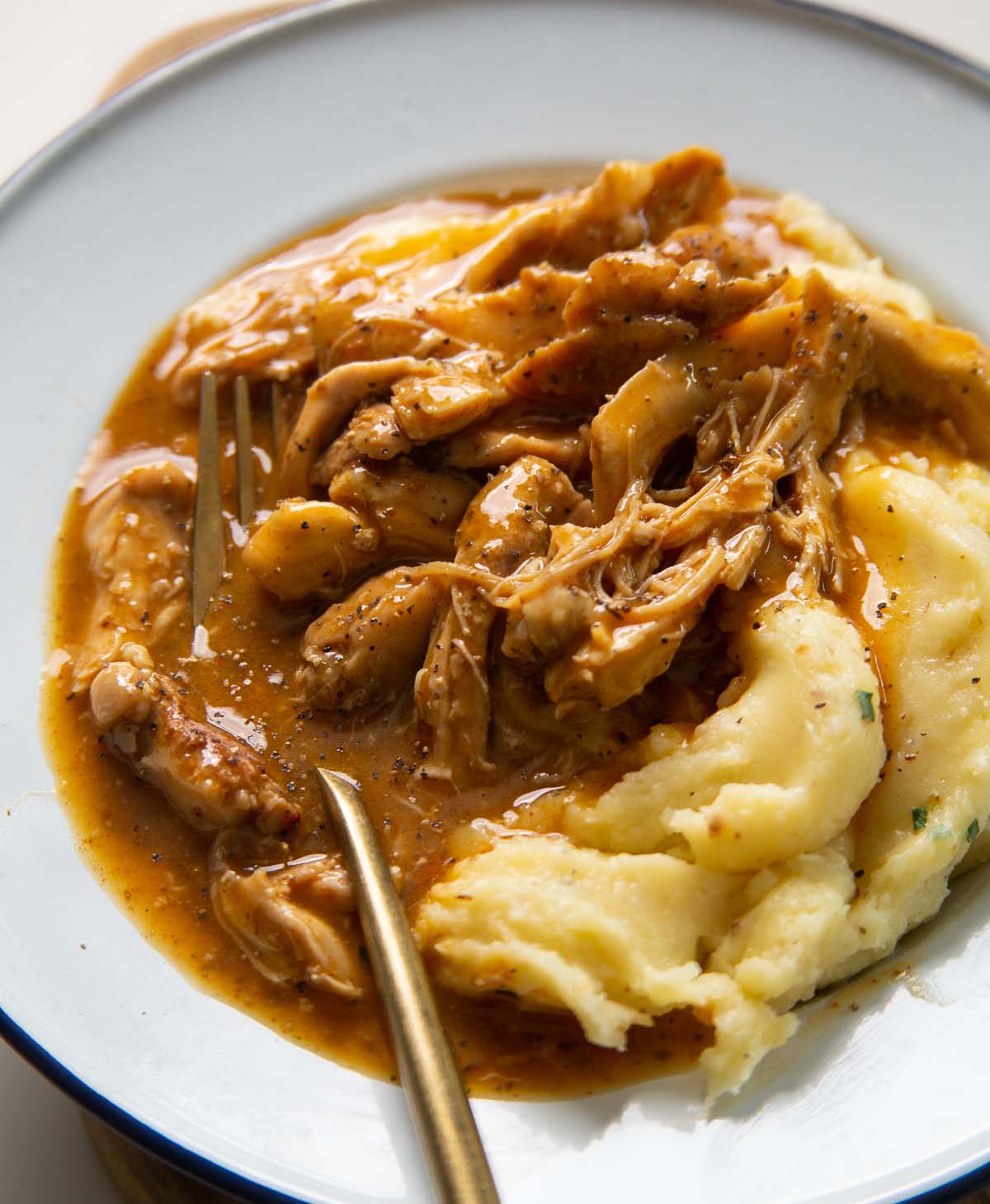 close up shot of chicken and gravy served with mash in white dish with gold fork