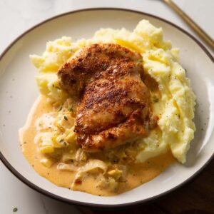 chicken thigh on mashed potato with leek sauce on small white plate