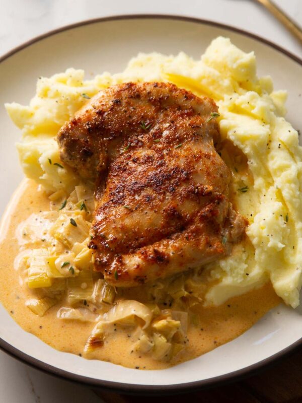 chicken thigh on mashed potato with leek sauce on small white plate