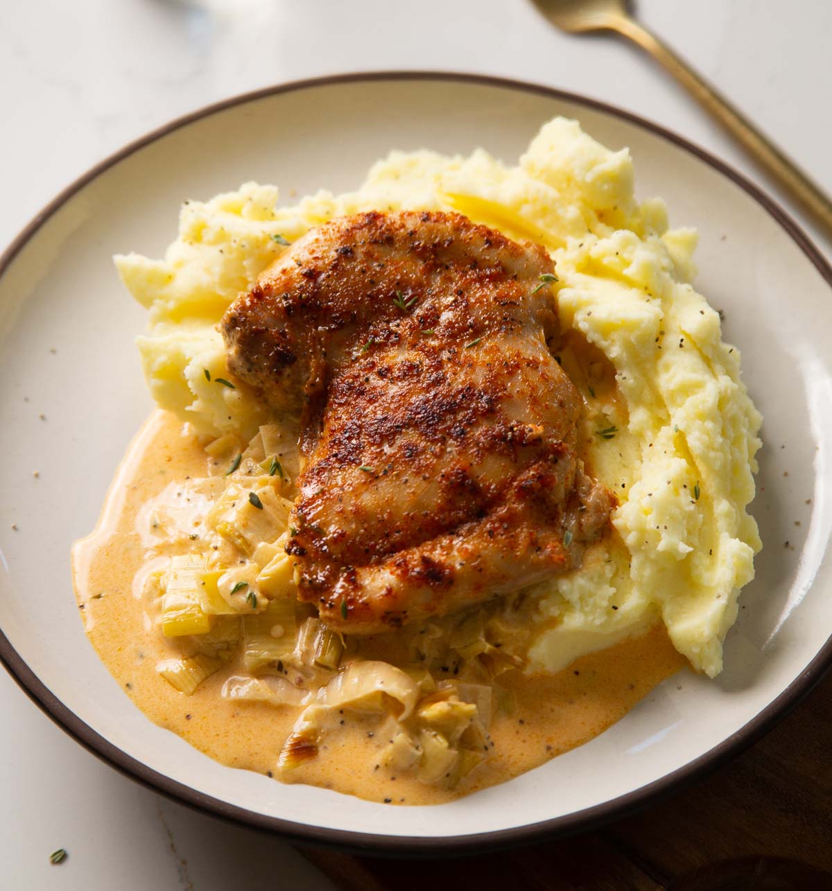 chicken thigh on a bed of mashed potato with leek sauce on small white plate